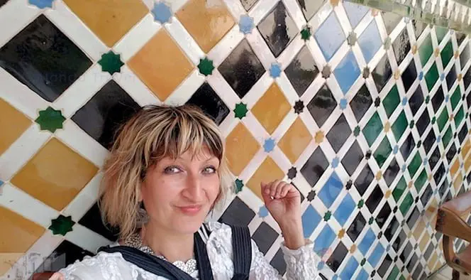 The author Alonga Travel in front of wall of colorful yellow & black tiles with arabesque patterns