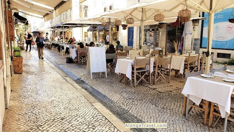 Cobblestone street lined up with restaurant tables and overhead umbrellas in Baixa area of Lisbon