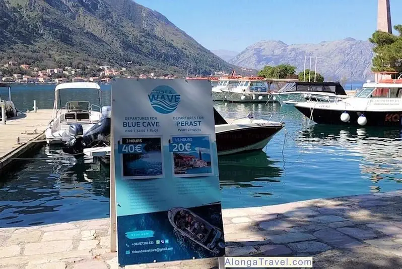A sign by the bay with boats saying: 'Blue cave tour'