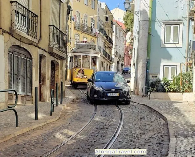 Cute yellow tram 28 follows winding tracks on a street un Lisbon