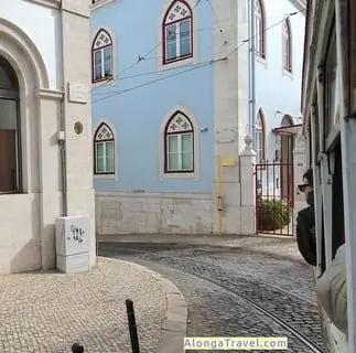 Trams starts a sharp turn in front of a blue house on a narrow street