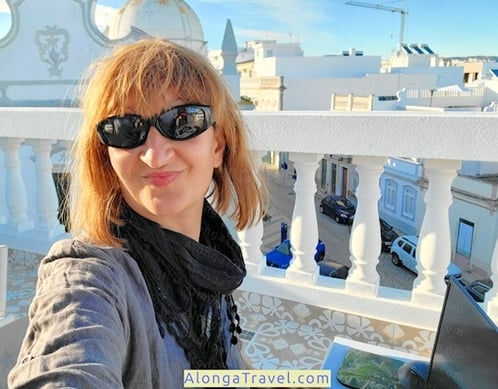 Alonga Travel the author smiles while working on her laptop in her mobile rooftop office in Portugal overlooking a church with a stork nest