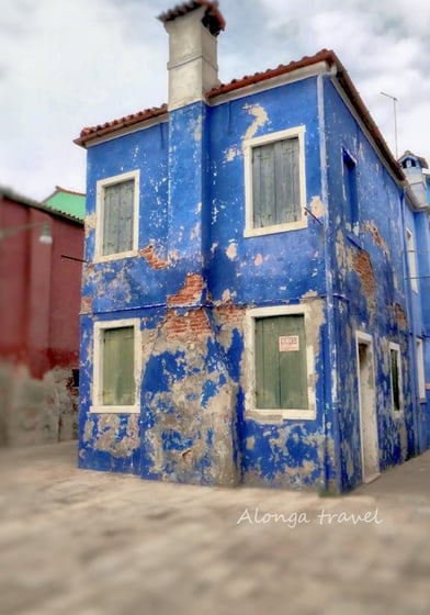Cute bright blue old building with pilled painting on Burano island in Venice