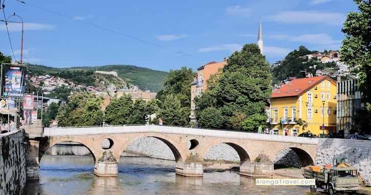 an ancient bridge over the river in Sarajevo with beautiful houses along the river & on the hill
