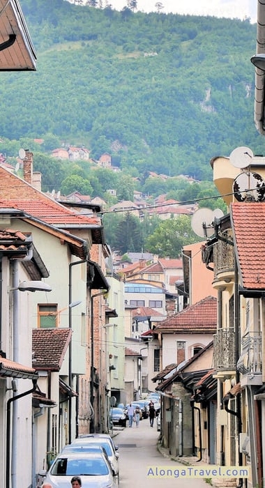 Tall 🗻 as a backdrop to a narrow pretty old street of Sarajevo - a cheap destination to visit